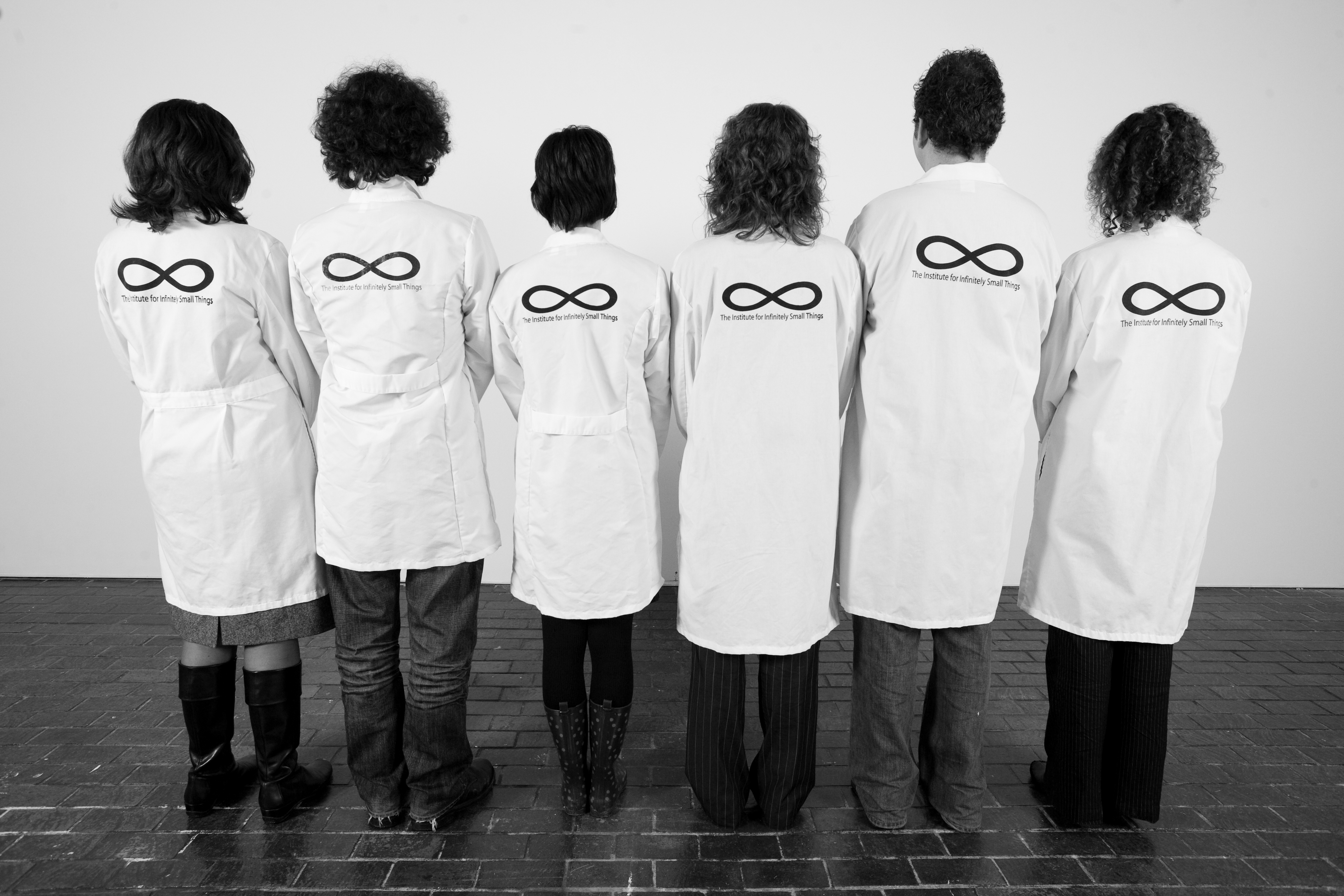 Members of the Institute stand with their backs to the camera, wearing their lab coats in a black and white image.